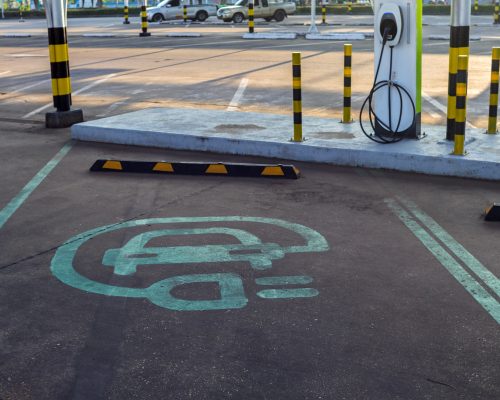 Electric vehicle charging symbol painted on parking lot asphalt. Clear, minimal design indicating EV charging station location.
