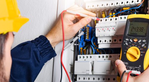 Electrician installing electric cable wires of fuse switch box. Multimeter in hands of electricians detail.