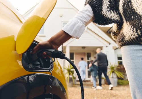 Woman plugging electric charger into car outside Home With Family