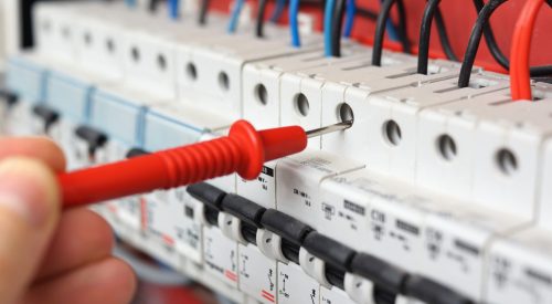 Hand of an electrician with multimeter probe at an electrical switchgear cabinet